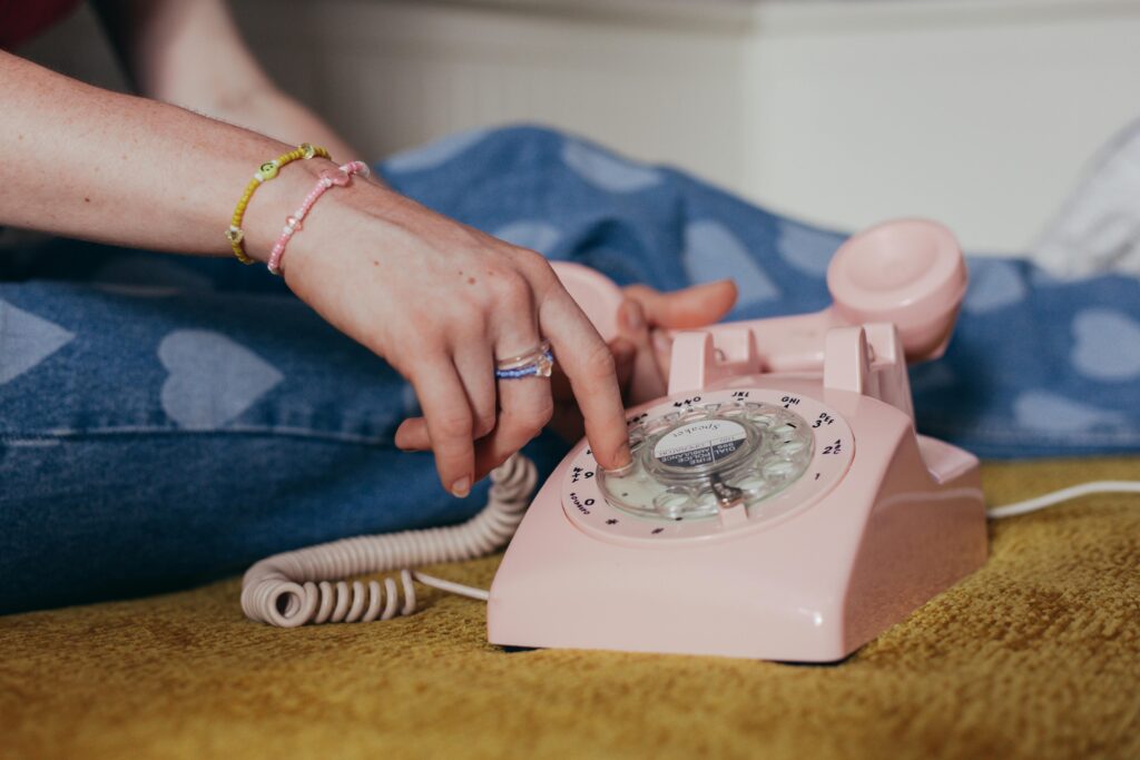 Close-up of a person dialing on a pink rotary phone, evoking a sense of nostalgia and retro charm.